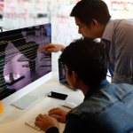 two computer programmers working with code on a laptop