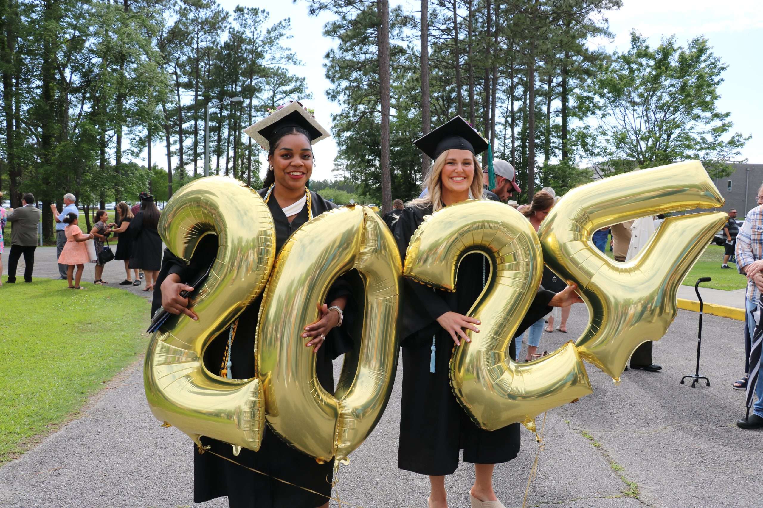 Two BCC Graduates holding giant 2024 balloons