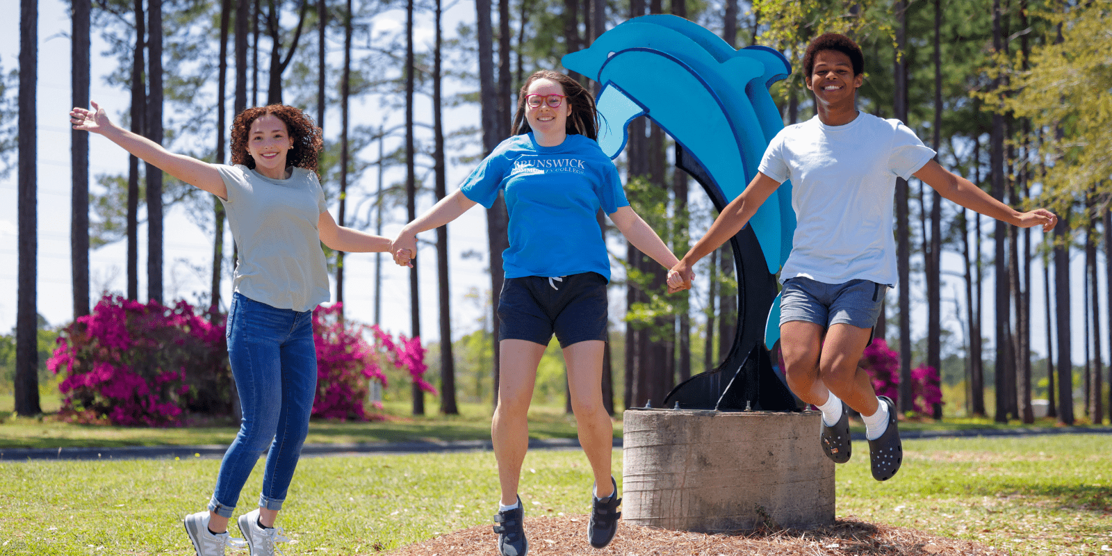 Three students jumping in front of the dolphin statue