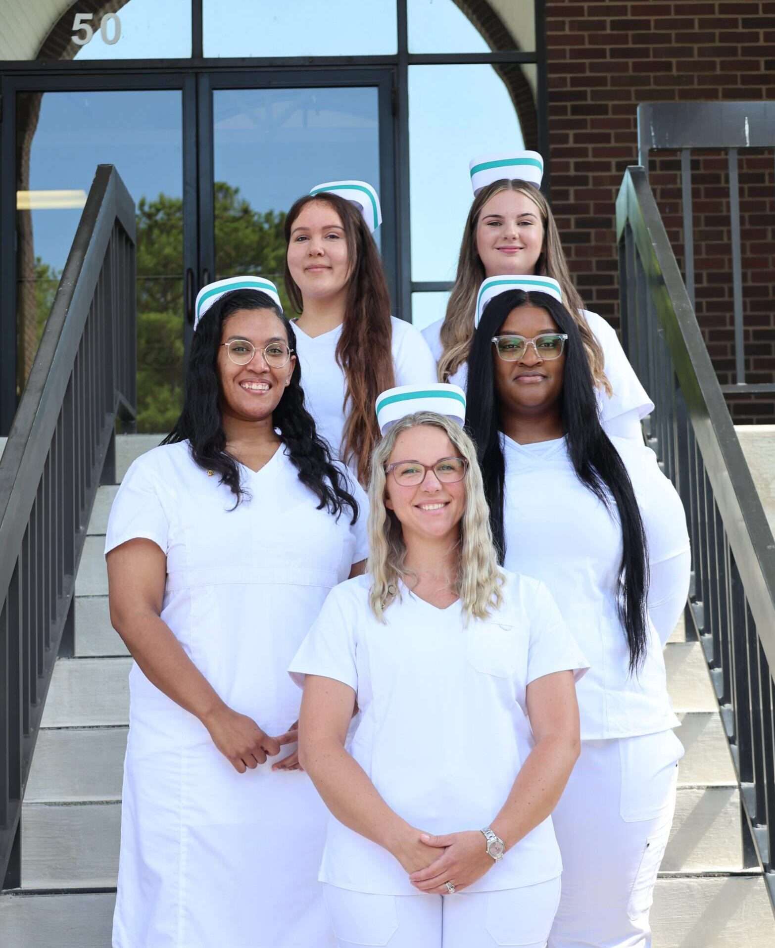 Five PN Graduates from the July 2025 class posing for a photo on Building A steps
