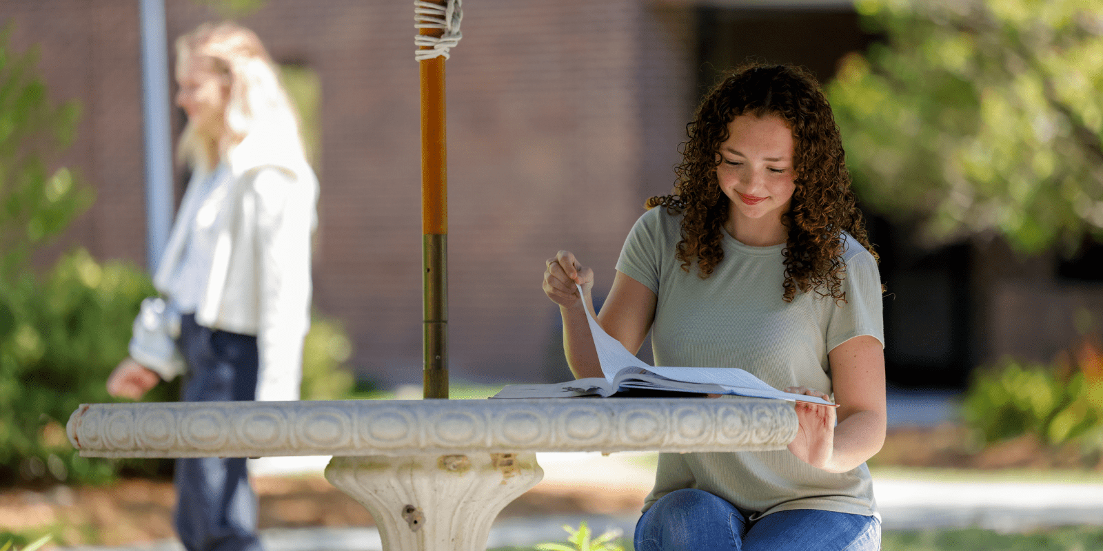 Student sitting at a table in the courtyard as another one passes by