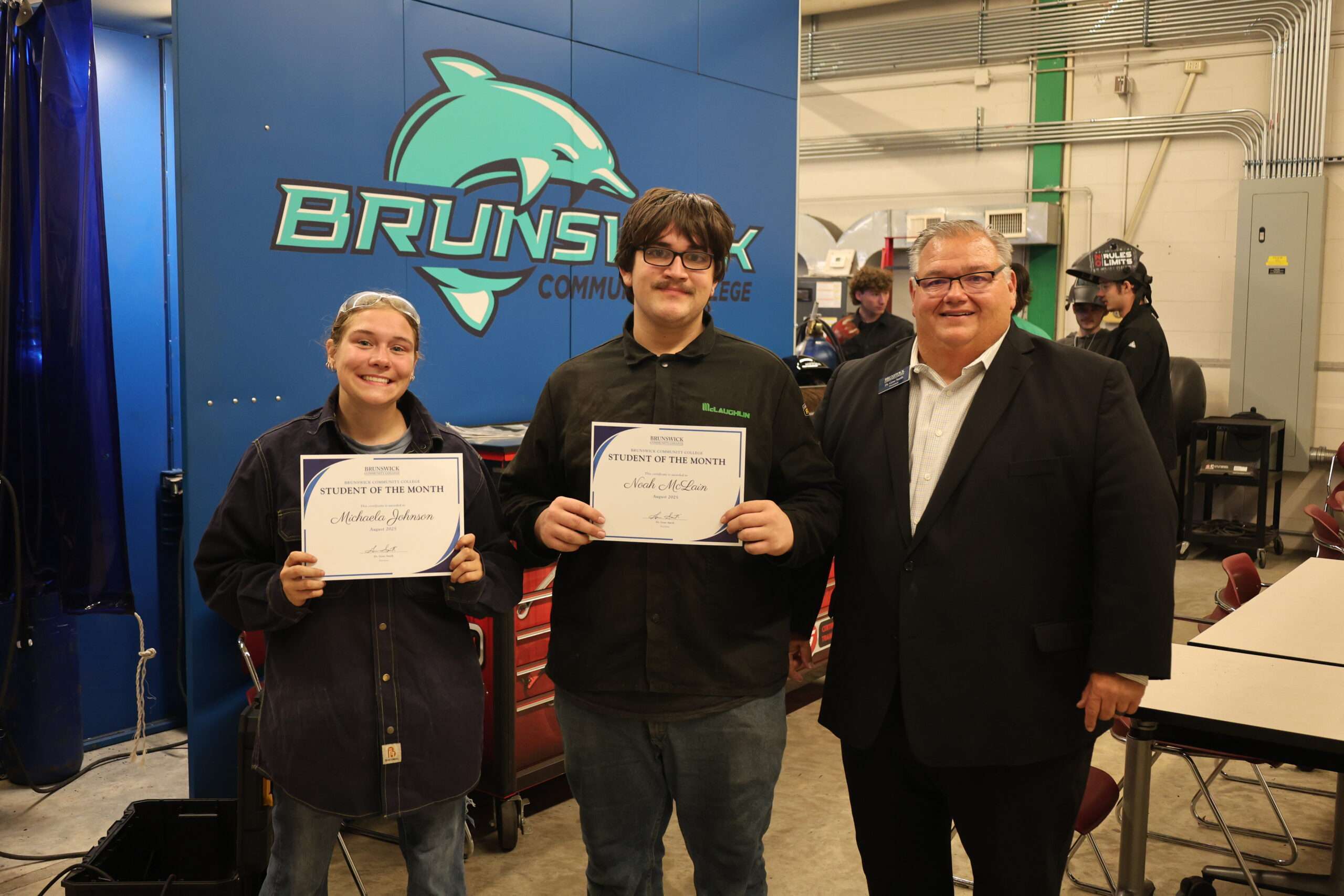 Two welding students in welding lab with President Smith during a student of the month presentation