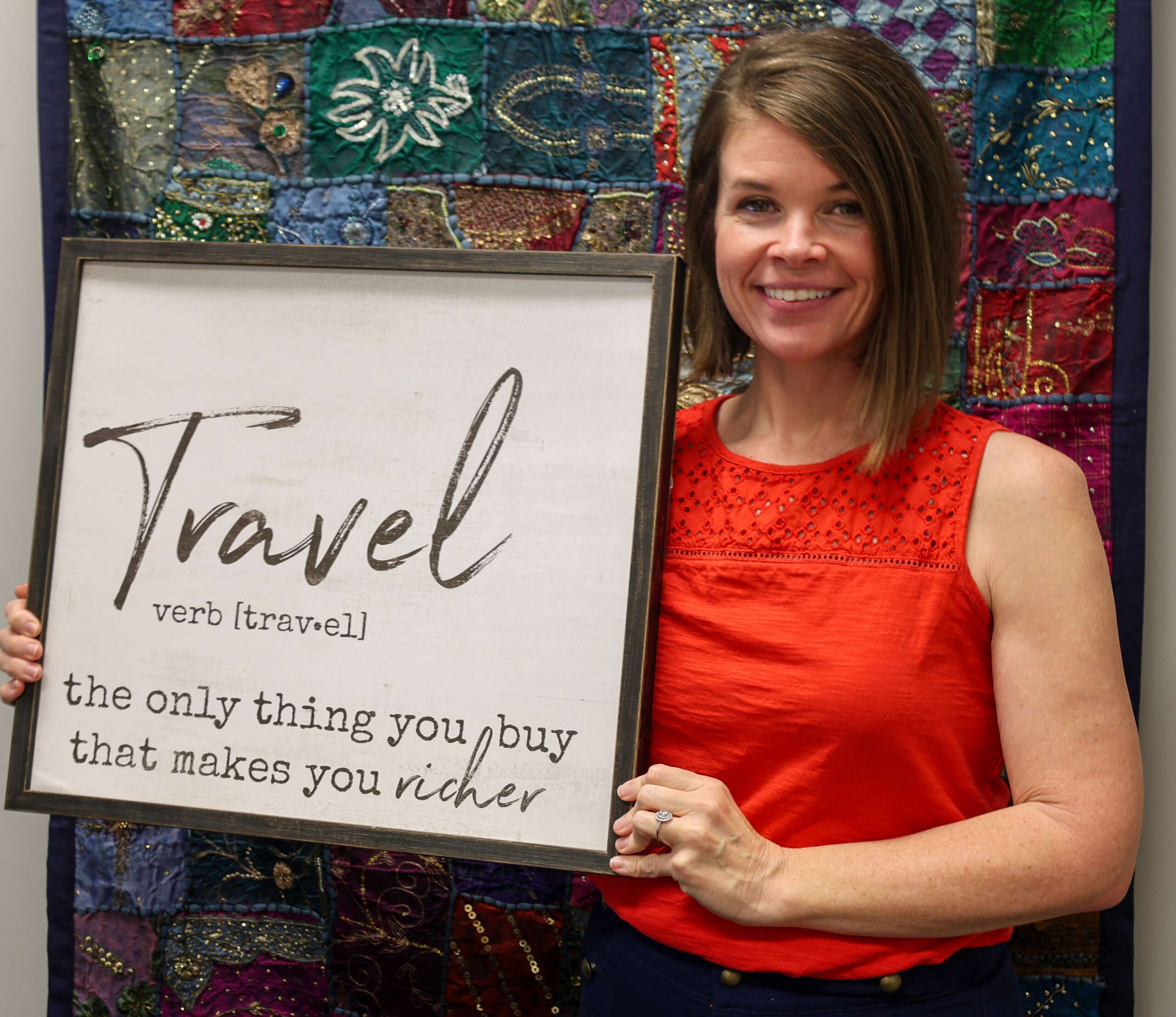 woman in red shirt standing in front of a colorful wall hanging and holding a sign