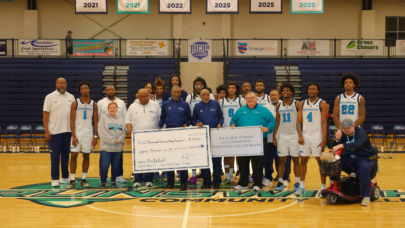 The Stanley brothers surrounded by BCC Leadership, Basketball Coaches, and Basketball team during a check presentation