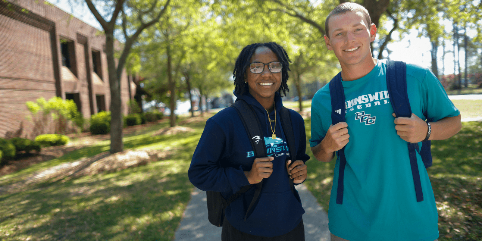 A male and female student smiling in a tree-lined campus setting